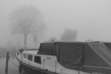 Ein Hausboot mit dem Namen „Sebas“ liegt vertäut im nebligen Hafen, dahinter sind Bäume schemenhaft zu erkennen. Marina de Domp in Sneek