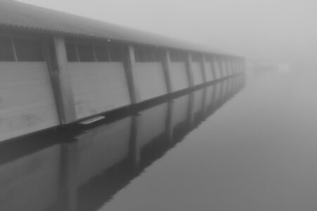 Eine lange Bootshalle spiegelt sich im nebligen Wasser eines ruhigen Hafens. Marina de Domp in Sneek