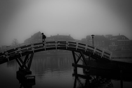 Ein Mann steht allein auf der gewölbten Holzbrücke, im Hintergrund verschwimmen Altstadthäuser im Nebel. in Sneek