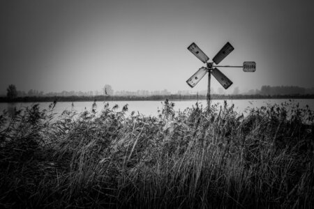 Eine alte Windrichtungsanzeige mit der Aufschrift „Record“ steht vor einem nebligen Seeufer mit Schilf.