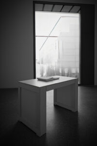 Minimalistischer weißer Tisch vor hellem Durchgang, dunkler Vordergrund, geometrische Architektur im Folkwang Museum Essen