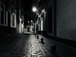 Menschenleere Altstadtgasse in Sevilla bei Nacht mit Kopfsteinpflaster und Straßenlaterne, tiefe Schwarzweiß-Kontraste