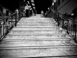 Breite Marmortreppe bei Nacht von unten fotografiert mit wenigen Personen, harte Kontraste, Schwarzweiß-Nachtaufnahme Sevilla