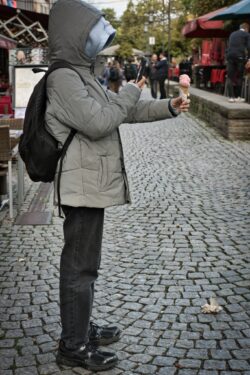 Eine Person in Winterkleidung fotografiert ihr Speiseeis mit dem Smartphone auf einer Pflasterstraße.