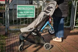 Ein Kinderwagen steht vor einem Schild mit der Aufschrift Notausgang Diese Tür darf nicht zugestellt werden.