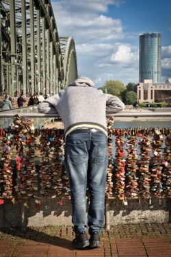 Ein Mann lehnt sich über das Geländer der Kölner Hohenzollernbrücke voller Liebesschlösser.